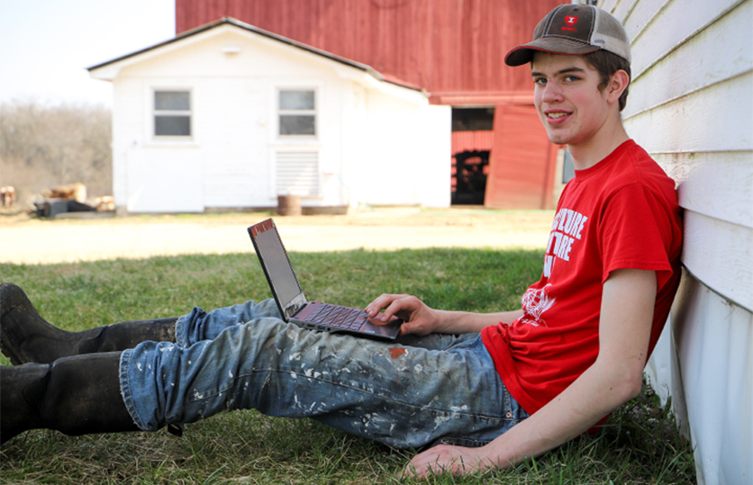 male student sitting outside using laptop