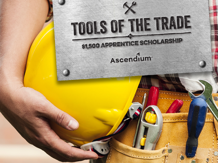 Piece of metal reads Tools of the Trade Scholarships, Ascendium. Held be a person wearing a tool belt