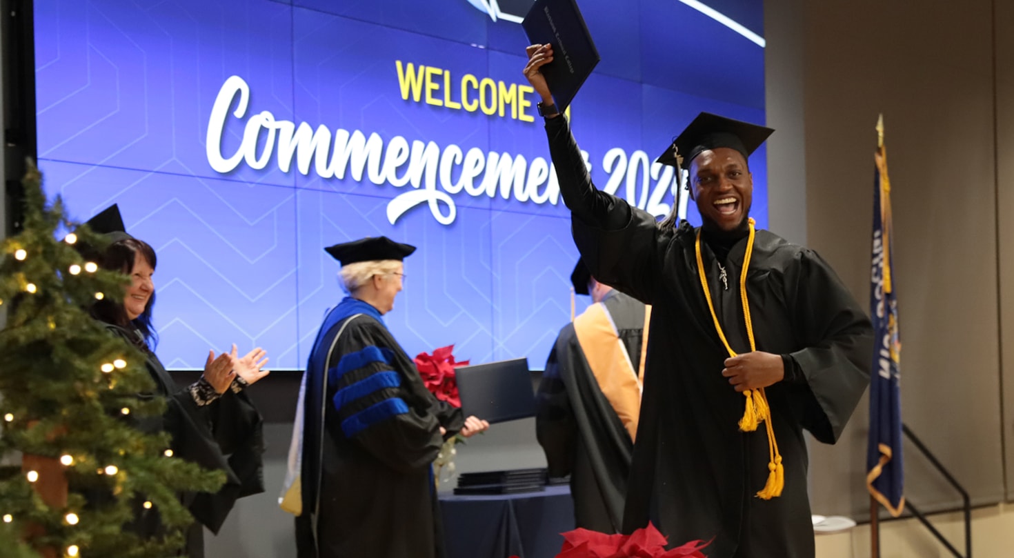 Graduate holding up diploma and smiling durring commencement ceremony