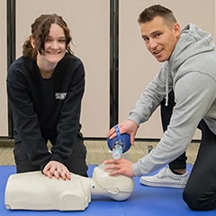 Two students performing CPR on a dummy looking at the camera